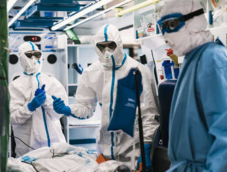 Group of professional doctors in protective uniform standing in ambulance car with equipment and preparing for patient transportation - ADSF11243