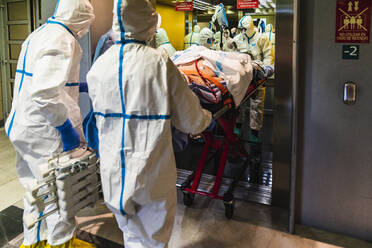 Gruppe von nicht erkennbaren Ärzten in Schutzkleidung, die einen Patienten mit einem Virus aus einem Aufzug im Krankenhaus holen - ADSF11247