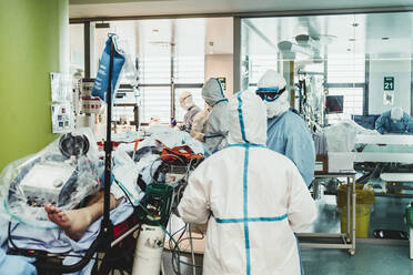 Nicht erkennbare professionelle Ärzte in Schutzanzügen und Masken, die sich um einen Patienten mit einer Virusinfektion kümmern, während sie im Operationssaal eines modernen Krankenhauses stehen - ADSF11250