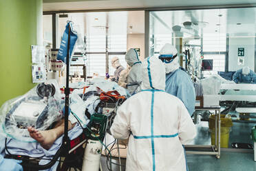 Unrecognizable professional doctors in protective uniforms and masks taking care of patient with viral infection while standing in operating room in modern hospital - ADSF11250