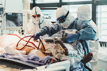 Nicht erkennbare professionelle Ärzte in Schutzanzügen und Masken, die sich um einen Patienten mit einer Virusinfektion kümmern, während sie im Operationssaal eines modernen Krankenhauses stehen - ADSF11252