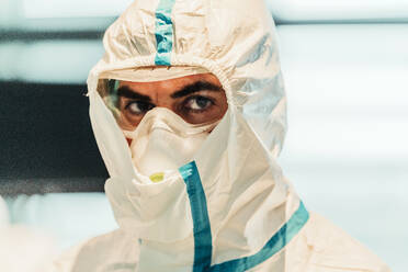 Portrait of serious professional doctor in protective uniform and mask standing in modern operating room and looking at camera - ADSF11255