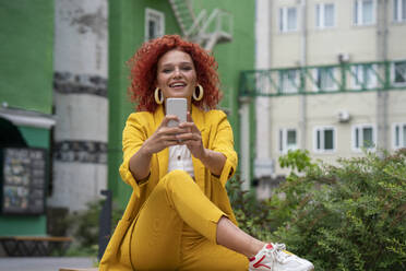 Businesswoman with curly hair, wearing yellow suit, taking smartphone selfie - VPIF02770