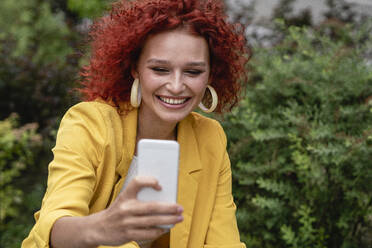 Businesswoman with curly hair, wearing yellow suit, taking smartphone selfie - VPIF02771