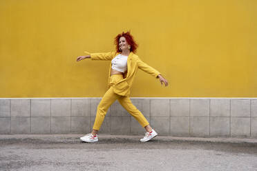 Energetic young woman in yellow suit running and jumping in front of yellow wall - VPIF02781