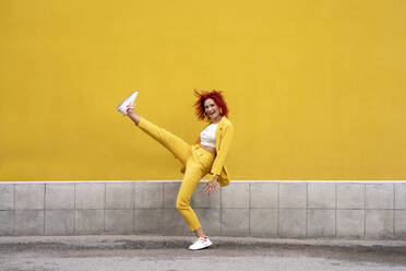 Energetische junge Frau in gelbem Anzug läuft und springt vor einer gelben Wand - VPIF02782