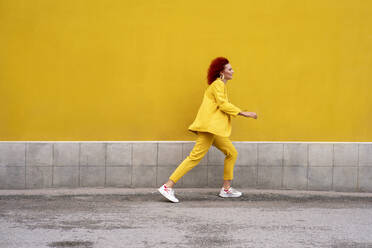 Energetische junge Frau in gelbem Anzug läuft und springt vor einer gelben Wand - VPIF02786