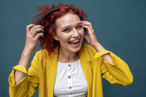 Junge Frau mit roten lockigen Haaren, die Kopfhörer trägt und Spaß am Musikhören hat, lizenzfreies Stockfoto