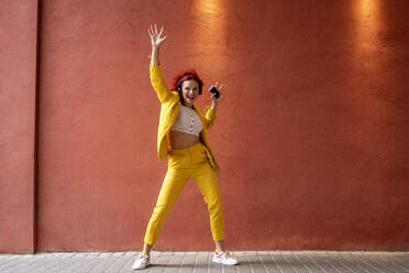 Junge Frau im gelben Anzug trägt Kopfhörer und tanzt zu Musik von ihrem Smartphone - VPIF02806