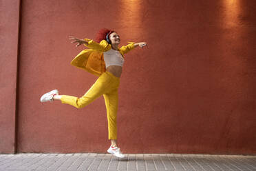 Young woman in yellow suit wearing headphones, dancing to music from her smartphone - VPIF02809