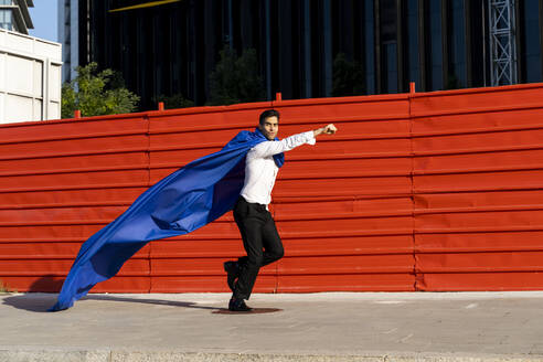 Businessman wearing superhero cape running on pavement - AFVF06921