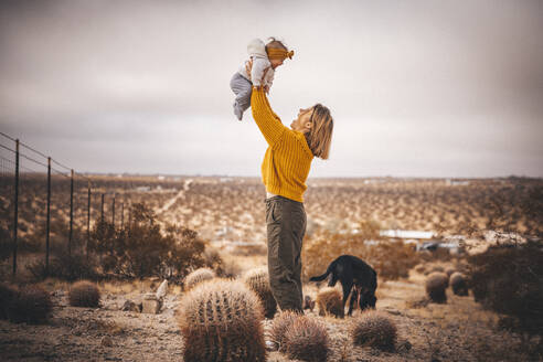 Eine Frau mit einem Baby und einem Hund steht in der Wüste von Kalifornien - CAVF88391