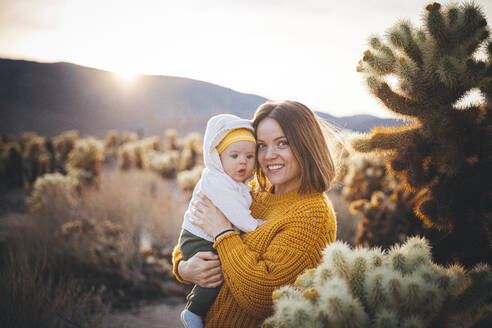 Eine Frau mit einem Baby steht in der Nähe eines Kaktus in der Wüste - CAVF88401