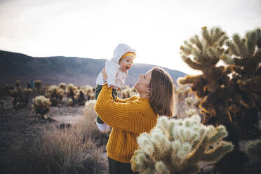 Eine Frau mit einem Baby steht in der Nähe eines Kaktus in der Wüste - CAVF88403