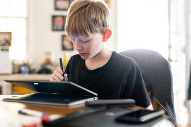 Teen working with 2in1 laptop computer at table inside home - CAVF88426