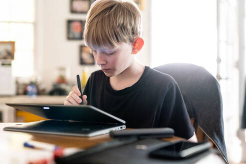 Teenager bei der Arbeit mit einem 2in1-Laptop-Computer am Tisch im Haus - CAVF88426