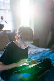 Tween zeichnet auf Tablet mit Stift, während sie auf dem Bett sitzt - CAVF88429