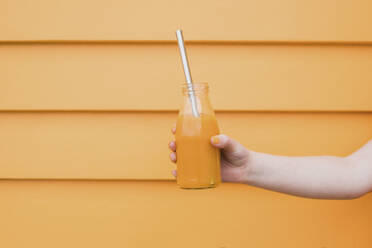 Mädchen hält eine mit Orangensaft gefüllte Glasflasche mit einem Metallstrohhalm - CAVF88442