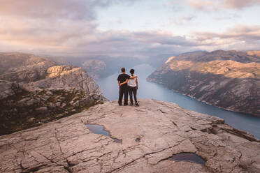 Couple standing at cliff at Preikestolen, Norway during sunset - CAVF88470