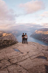 Couple standing at cliff at Preikestolen, Norway during sunset - CAVF88471