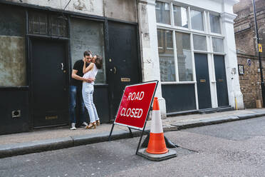 Zartes Paar in Freizeitkleidung steht in der Nähe von schäbigen Gebäude in der Stadt in der Nähe der Straße geschlossen Zeichen und umarmt während eines Spaziergangs in London - ADSF11387