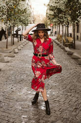 Junge Frau in stilvollem Kleid und Hut zu Fuß auf gealterten Bürgersteig in der Stadt Straße - ADSF11399