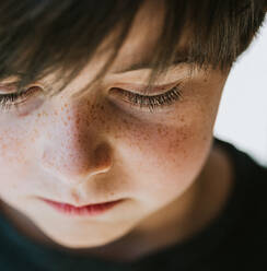 Nahaufnahme des Gesichts eines kleinen Jungen mit Sommersprossen, der nach unten schaut. - CAVF88496