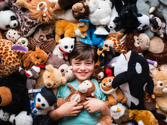 Happy young boy surrounded by his stuffed animals shot from above. - CAVF88502