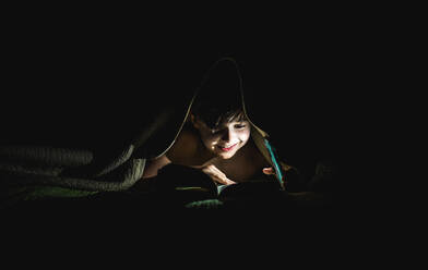 Young boy reading a book under a blanket using a flashlight. - CAVF88505