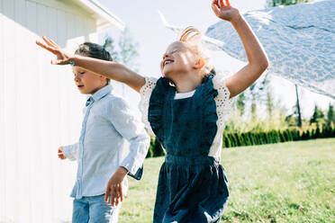 Girl and boy running through the washing on the line with great joy - CAVF88506