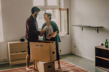 Hipster-Paar packt gemeinsam Kisten aus, während sie barfuß in einem hellen Raum stehen - ADSF11418