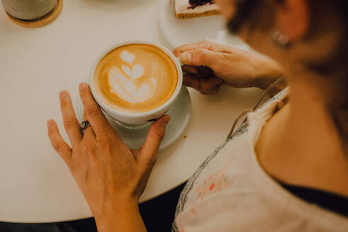 Erste Person-Ansicht einer Frau, die eine Tasse hält, während sie in einem modernen Café sitzt - ADSF11426