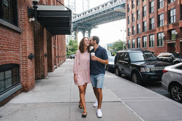 Sanftmütiger Freund mit Kaffee zum Mitnehmen umarmt lächelnde Freundin während eines Stadtspaziergangs in New York - ADSF11452