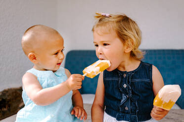 Süße kleine Mädchen essen leckeres Eis am Stiel, während sie den Sommer genießen und im Garten zusammensitzen - ADSF11457