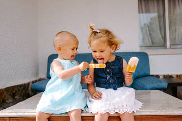 Süße kleine Mädchen essen leckeres Eis am Stiel, während sie den Sommer genießen und im Garten zusammensitzen - ADSF11458