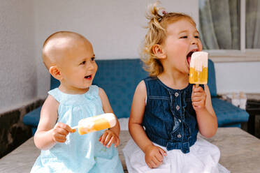 Süße kleine Mädchen essen leckeres Eis am Stiel, während sie den Sommer genießen und im Garten zusammensitzen - ADSF11459