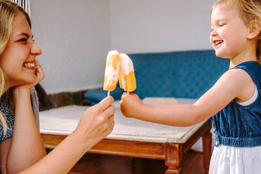 Side view of cheerful woman and little girl relaxing in courtyard in summer with homemade popsicles - ADSF11460