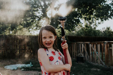 Young girl playing outside with spraying hose - CAVF88527