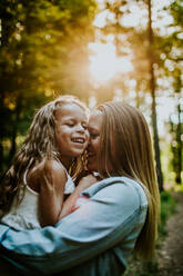 Glückliche Mutter und Tochter lachend und kuschelnd im beleuchteten Wald - CAVF88532