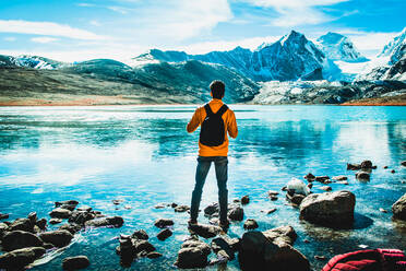 Man standing on a lake covered snow mountain - CAVF88536