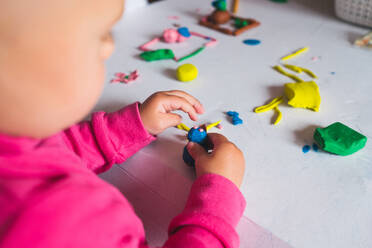 From above view of unrecognizable little child playing with colorful modelling clay on white table at home - ADSF11495