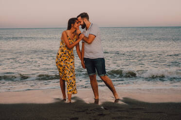 Amorous man hugging woman while charming lady looking gently at seaside - ADSF11499