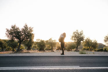 Side view of couple in love embracing on road on background of spectacular sunset and natural landscape - ADSF11504