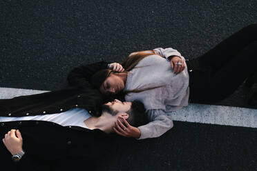 From above of gentle multiethnic couple relaxing on asphalt roadway while caressing faces and looking at each other - ADSF11505