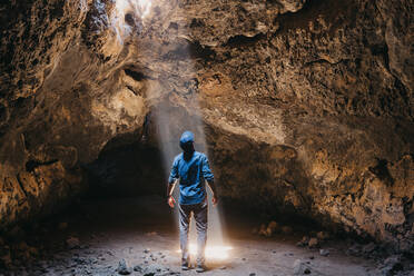 Man admires cascading light beam in lava cave - CAVF88551