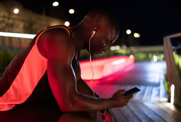 Schwarzer Läufer benutzt Smartphone auf Bank - CAVF88572
