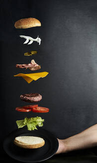 Leckerer Hamburger mit fliegenden Zutaten auf schwarzem Hintergrund - CAVF88581