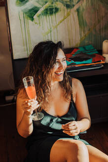 Frau mit einem Glas Wein auf dem Boden sitzend in einem Zimmer - CAVF88592