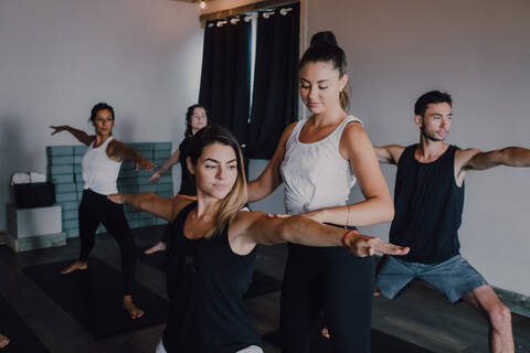 Smiling diligent female instructor in sportswear teaching warrior pose two group of sporty people doing exercise standing on sports mats in modern workout room stock photo