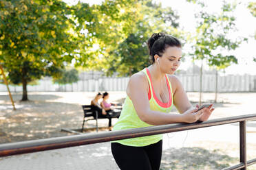 Frau benutzt Mobiltelefon im Park, Freunde machen Pause im Hintergrund - CUF56215